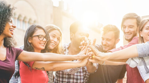 Eine Gruppe Freunde steht im Kreis, alle lächeln und halten die Hände in der Mitte zusammen