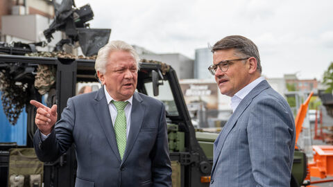 Ministerpräsident Rhein (rechts) und Vorstandsvorsitzender von Rheinmetall Armin Papperger (links) auf dem Werksgelände. Im Hintergrund stehen Geräte.