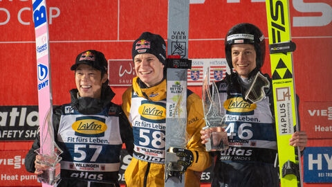 Andreas Wellinger, Ryoyu Kobayashi und Gregor Deschwanden stehen auf Siegertreppe mit Ski 