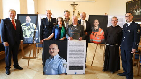 Mehrere Personen stehen in einem Raum, zwischen Ihnen Portraits von Einsatzkräften.