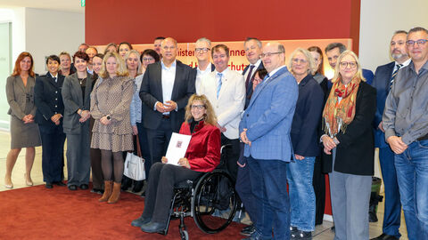 Über 20 Personen stehen nebeneinander auf einem roten Teppich und schauen in die Kamera.